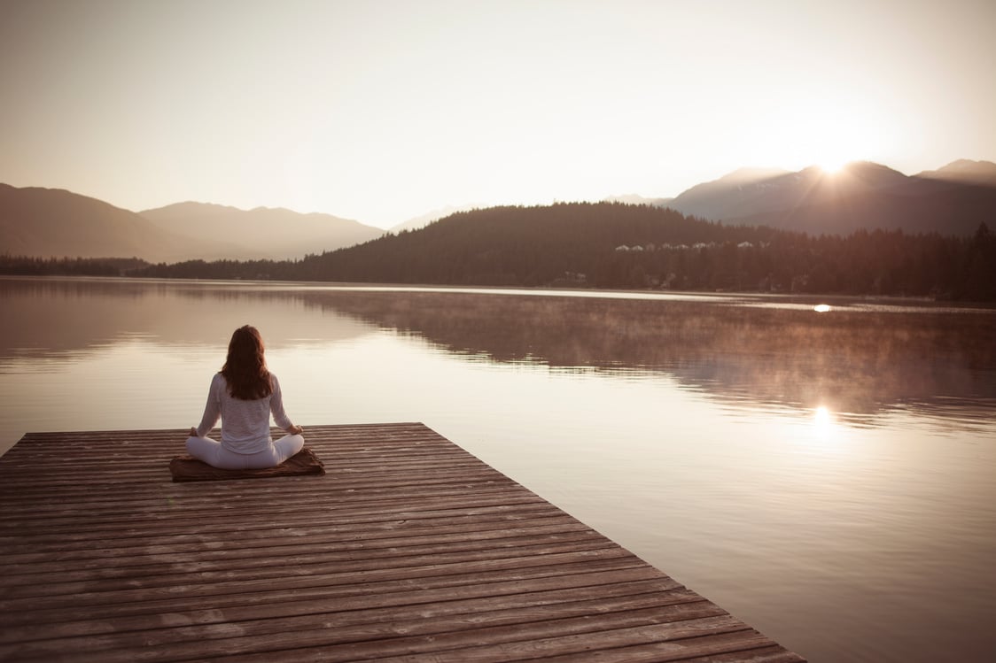 Woman meditating by lake.